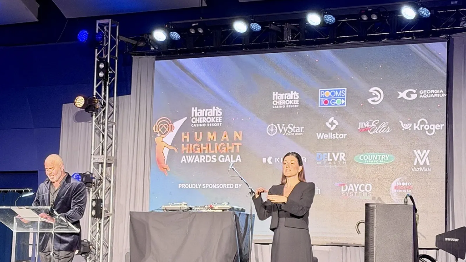 Man speaking at podium and woman signing on stage at Harrah's Cherokee Human Highlight Awards Gala.