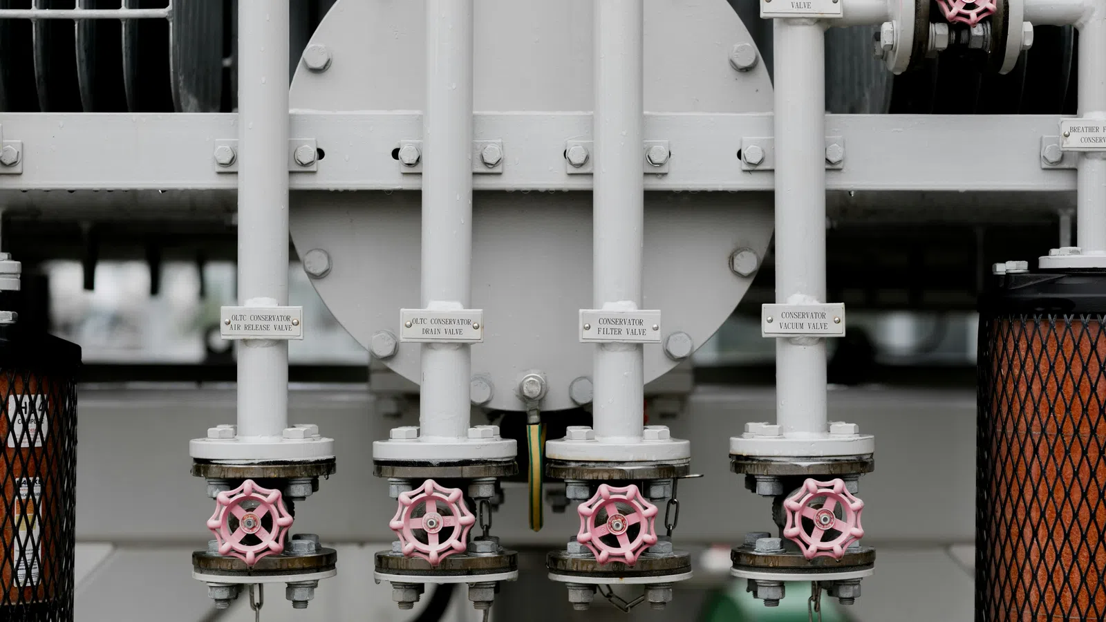 Close-up of industrial white metal pipes with pink valve handles and labeled tags in a factory setting.