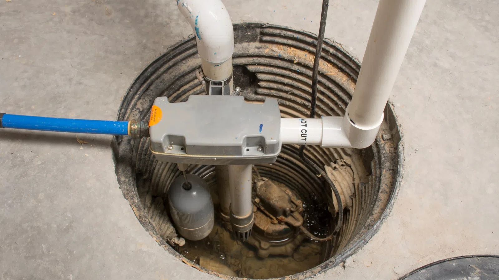 Sump pump installed in basement pit with connected pipes and wiring on concrete floor.