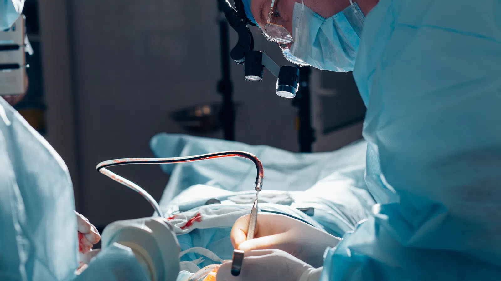 Surgeons in protective gear perform a precise operation in a sterile operating room under bright surgical lights.