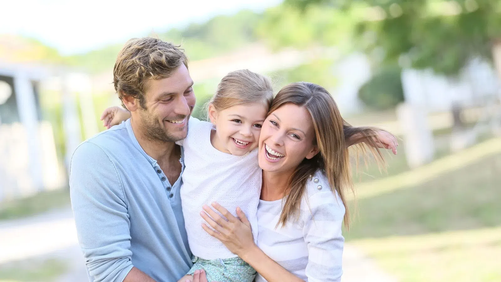 Happy family of three outdoors smiling and hugging in a sunlit park setting on a bright day