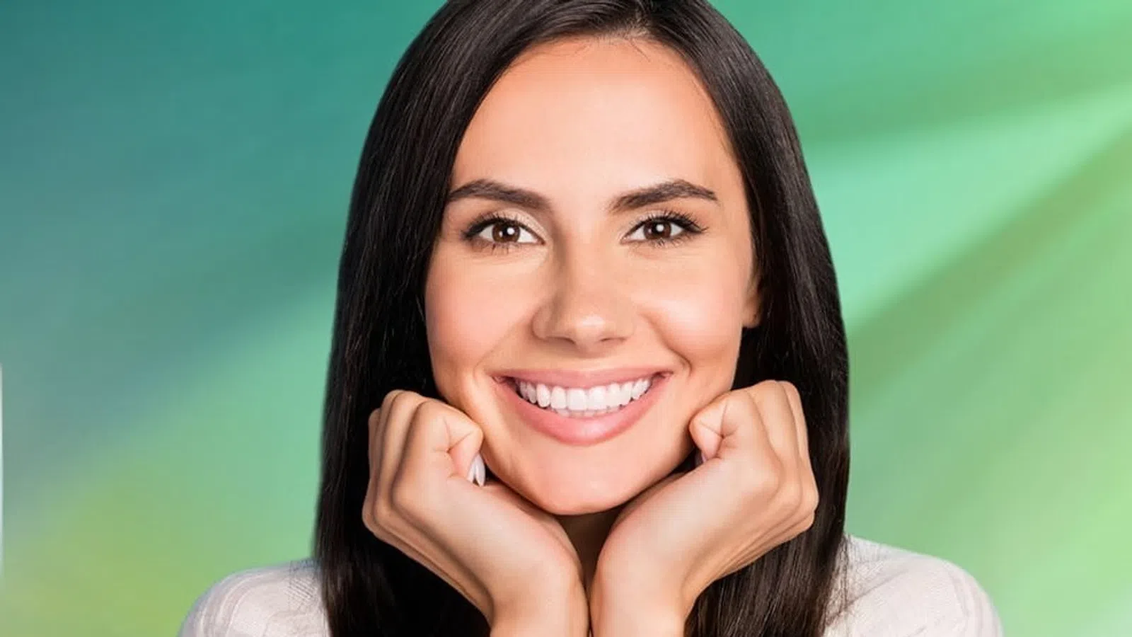 Smiling young woman with long dark hair resting face on hands against a green gradient background.