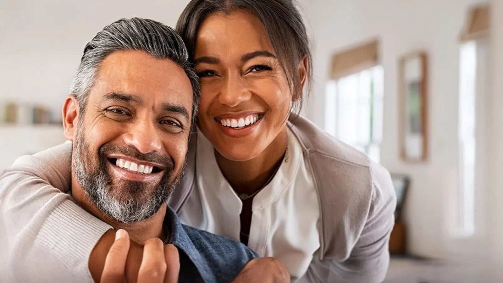 Happy couple smiling and embracing in a bright, cozy home setting with natural light.