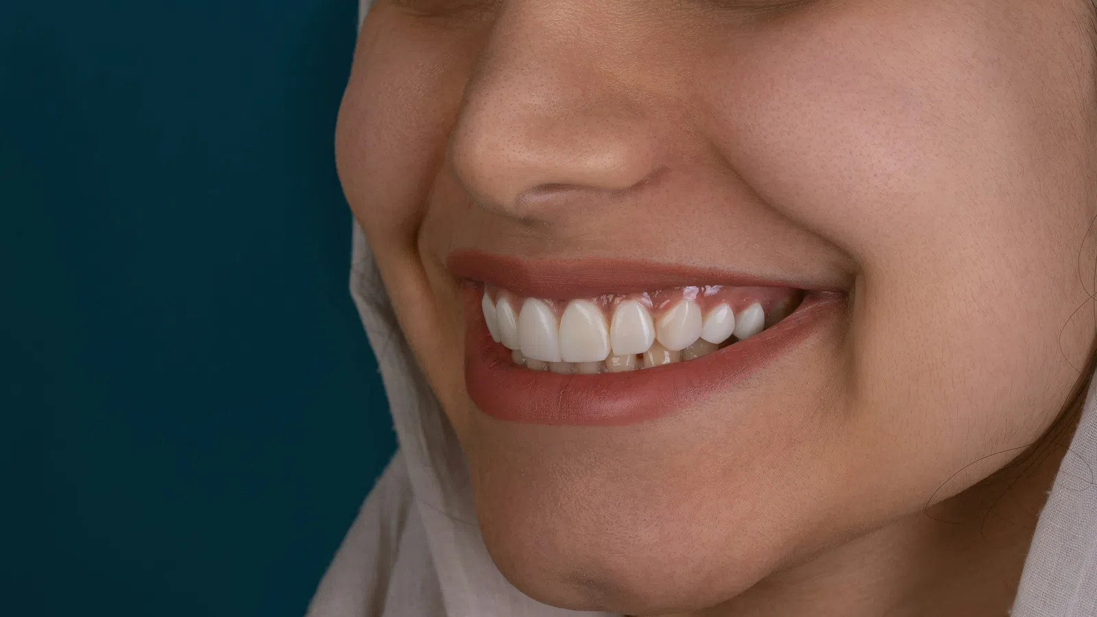 Close-up of a smiling woman with perfect white teeth and natural skin against a dark blue background.