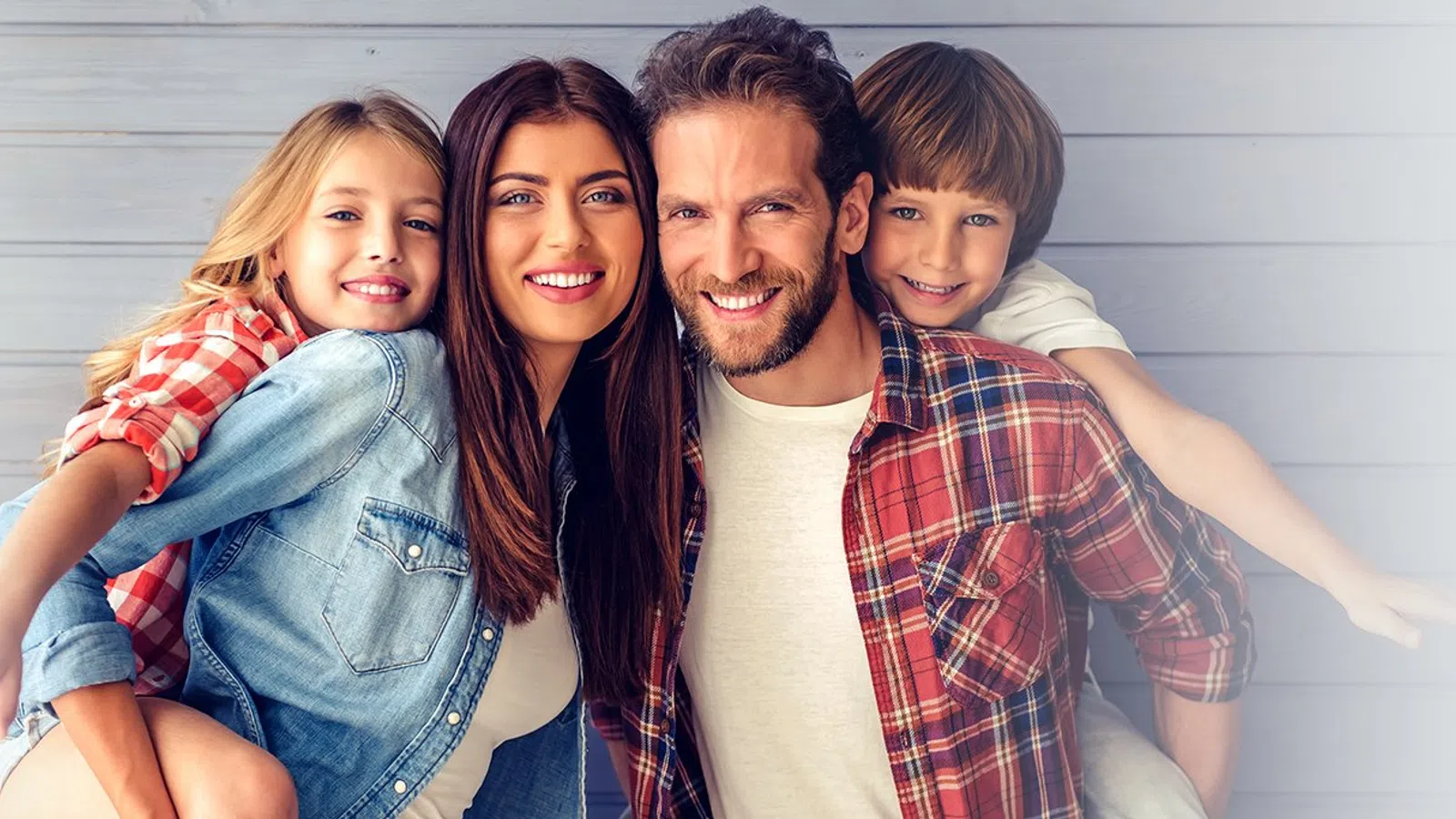 Smiling family of four with parents and children in casual clothes against wooden wall background