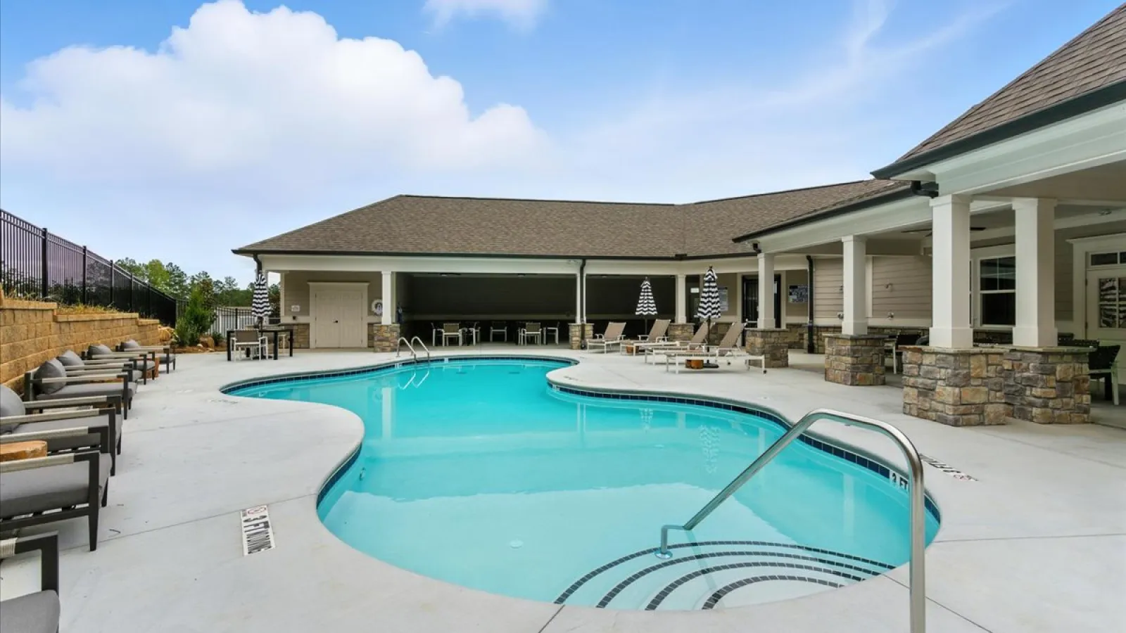 Outdoor swimming pool with lounge chairs, umbrellas, and covered patio area under blue sky