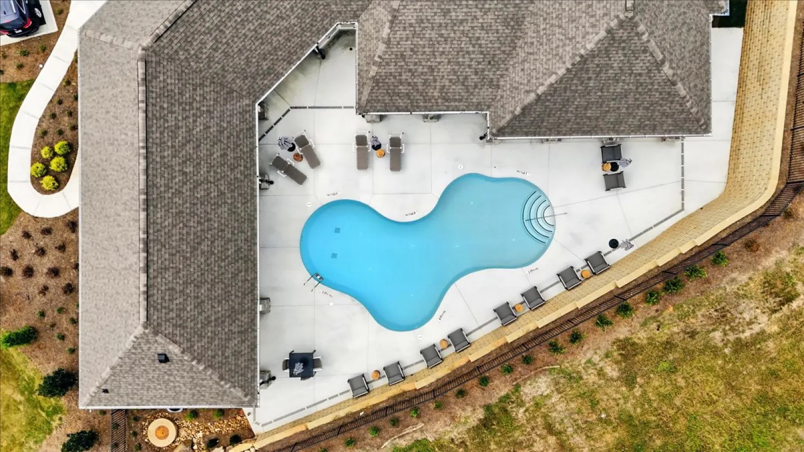Aerial view of a backyard swimming pool with patio chairs and shaded roof area surrounding it.