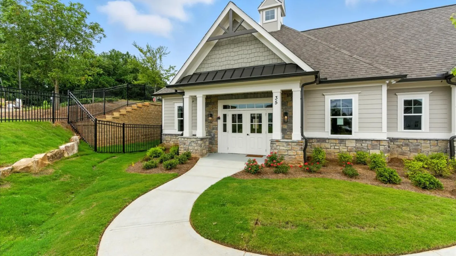 Modern single-story house with stone and siding exterior, white front door, curved concrete walkway, and landscaped lawn.