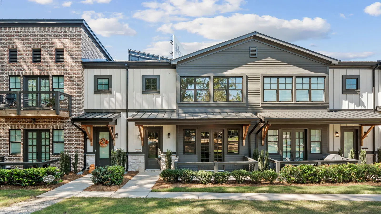 Modern townhouses with brick and siding exteriors, landscaped front yards, and clear blue sky in the background.