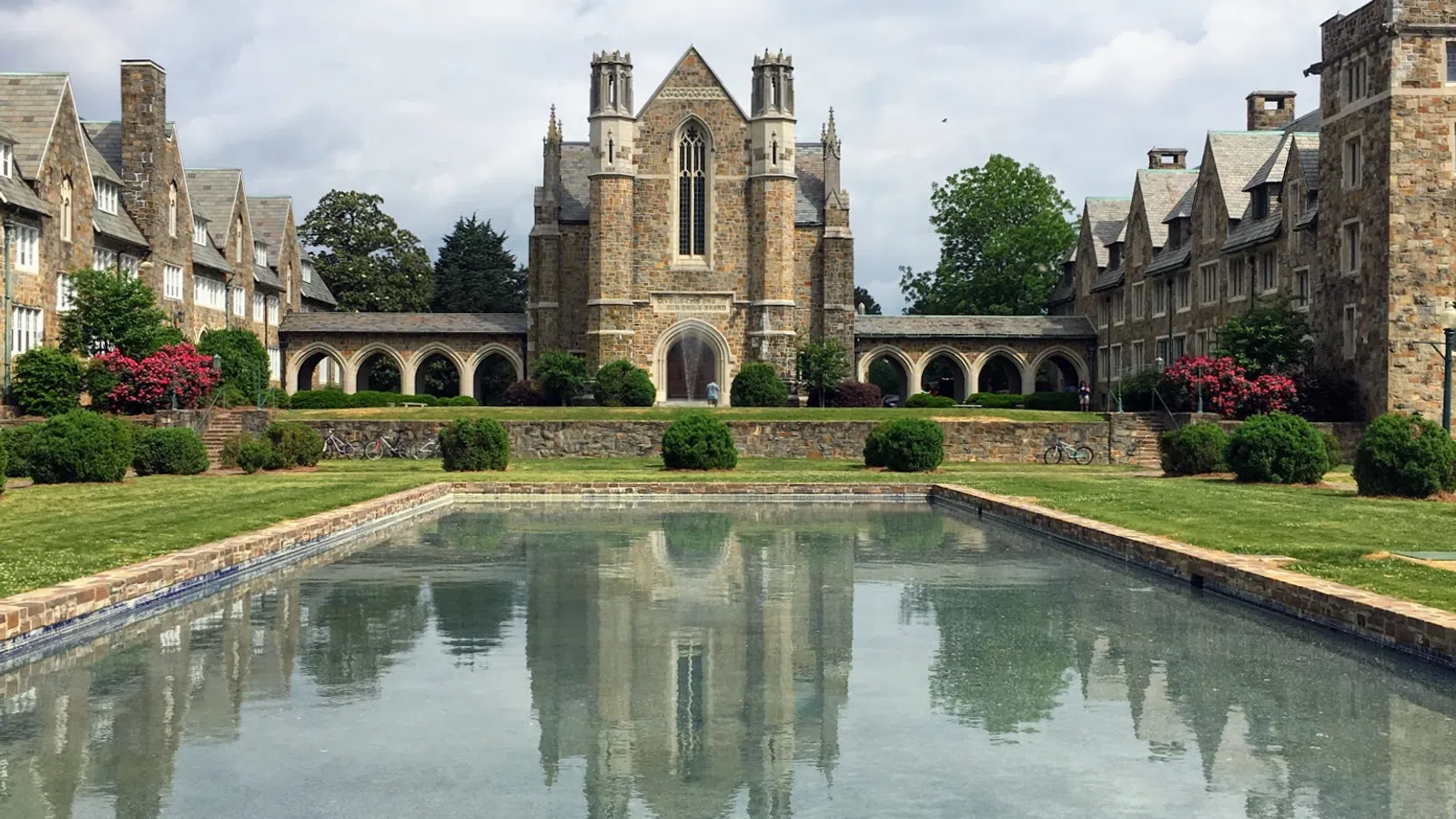 A historic building reflected in a serene pond surrounded by lush greenery and vibrant flowers.