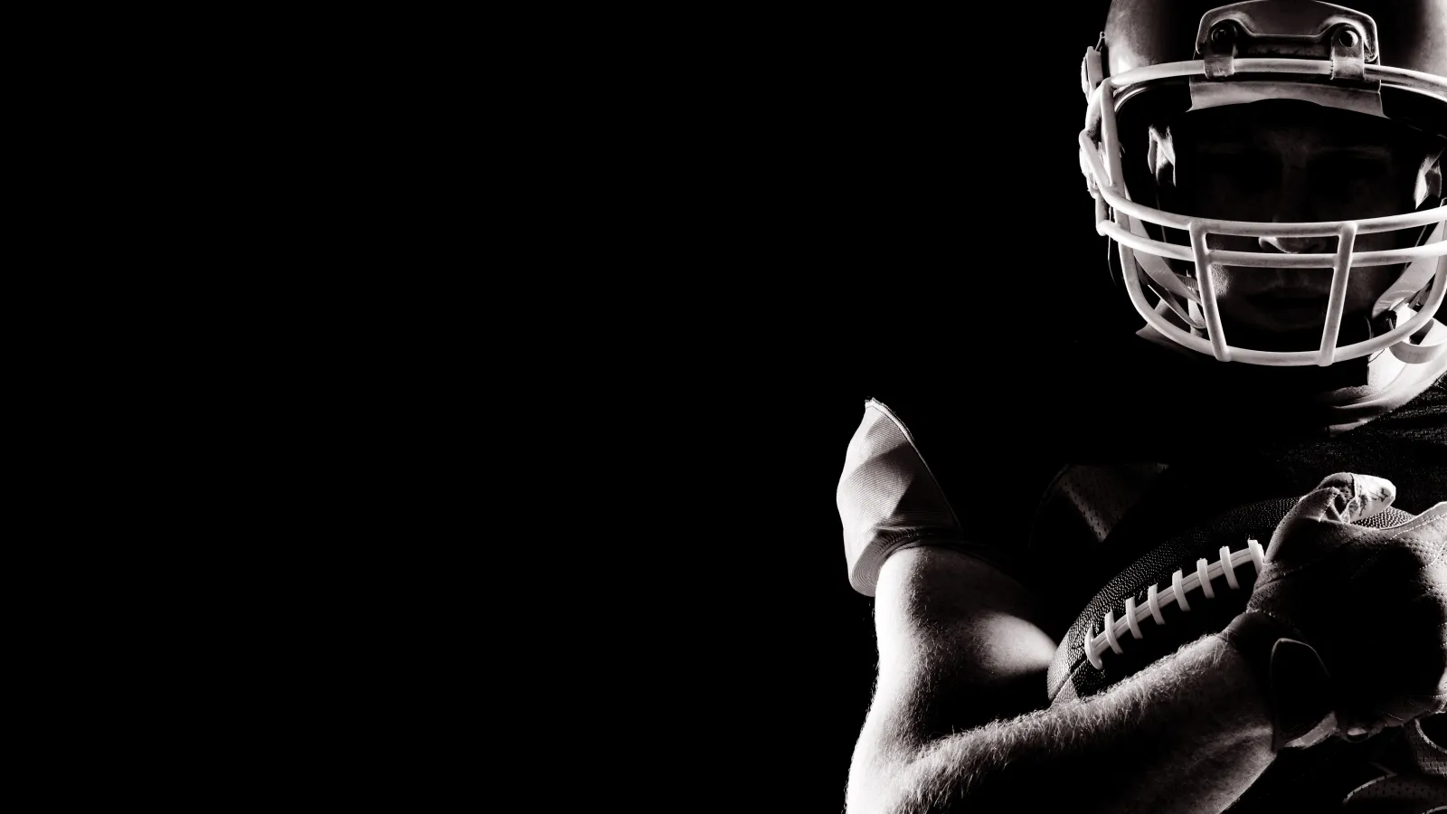 Silhouetted American football player holding ball against dark background with dramatic lighting