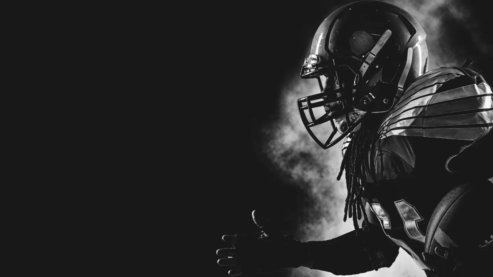 Black and white photo of an American football player in full gear running in profile with smoke behind him