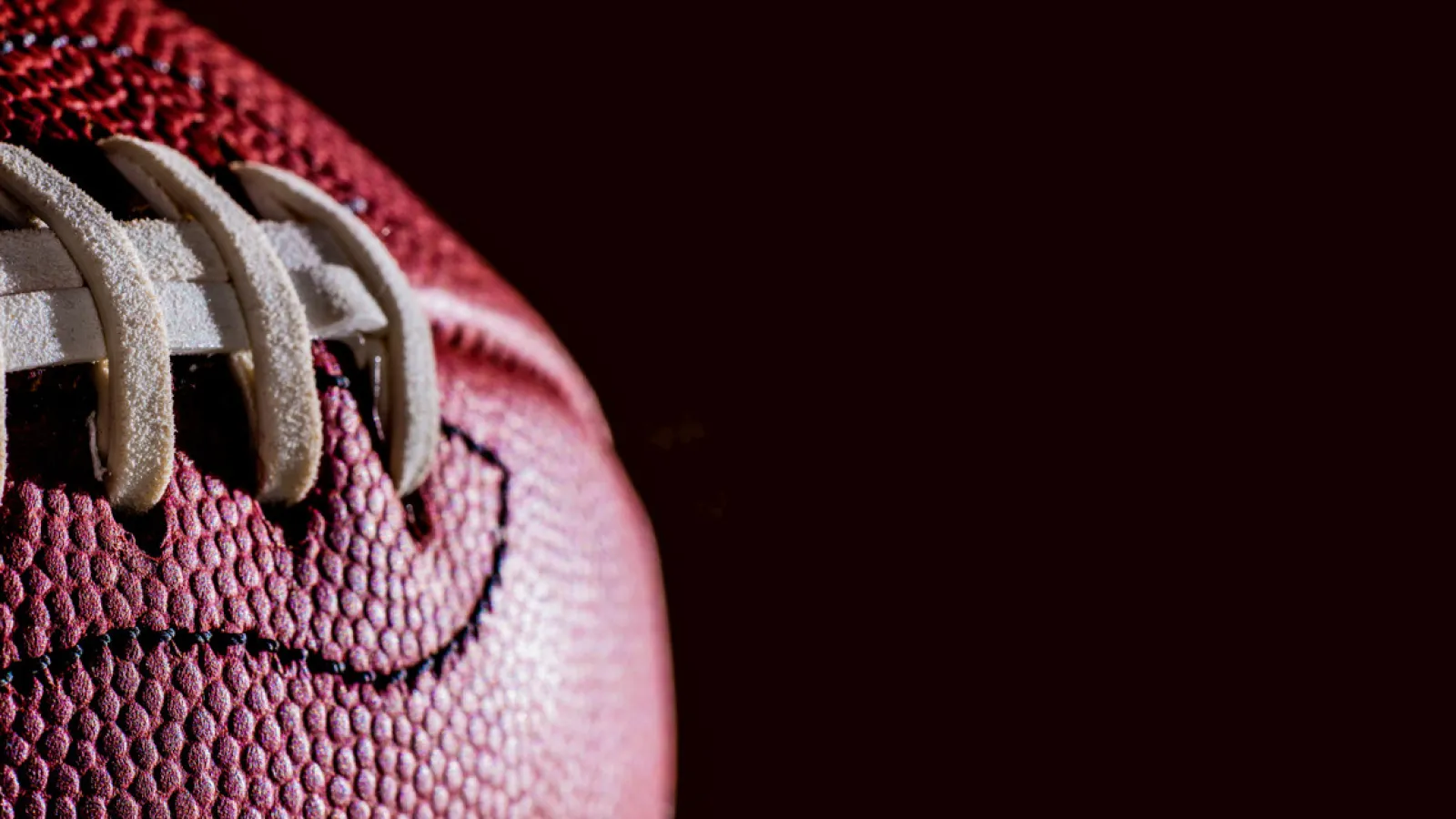 Close-up of a textured leather American football showing white laces and grain detail