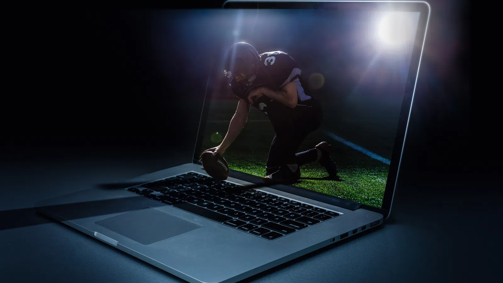 Football player emerging from laptop screen on a dark background with bright spotlight and lens flare effects
