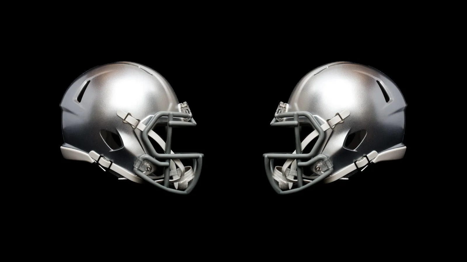 Two silver football helmets facing each other on a black background highlighting their design and structure