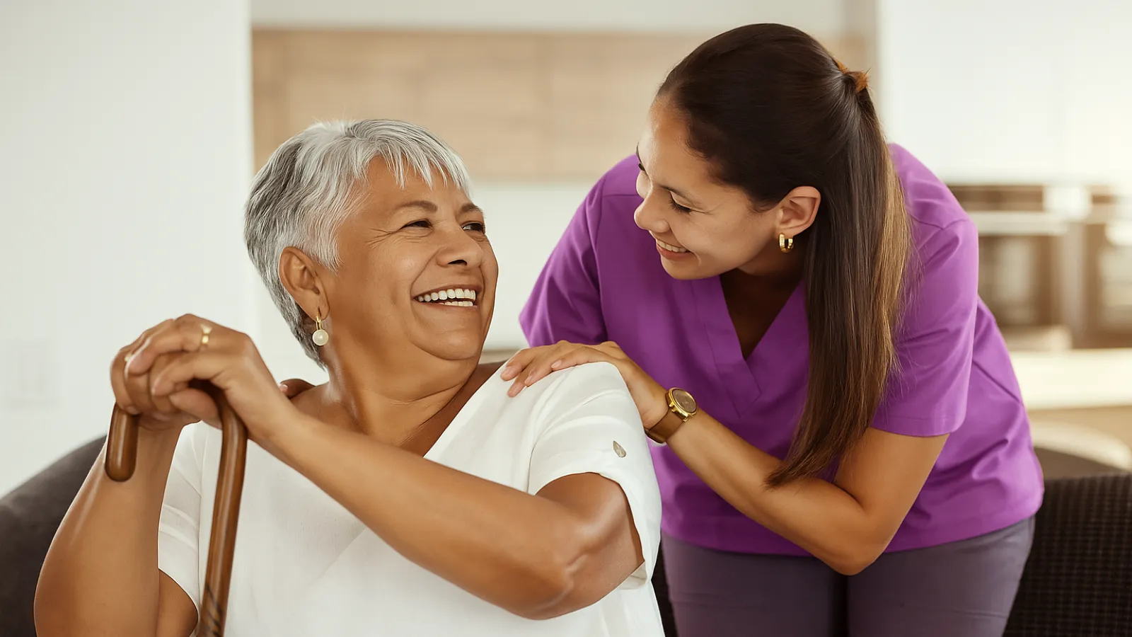 Elderly woman smiling while nurse in purple scrubs offers support and companionship at home.