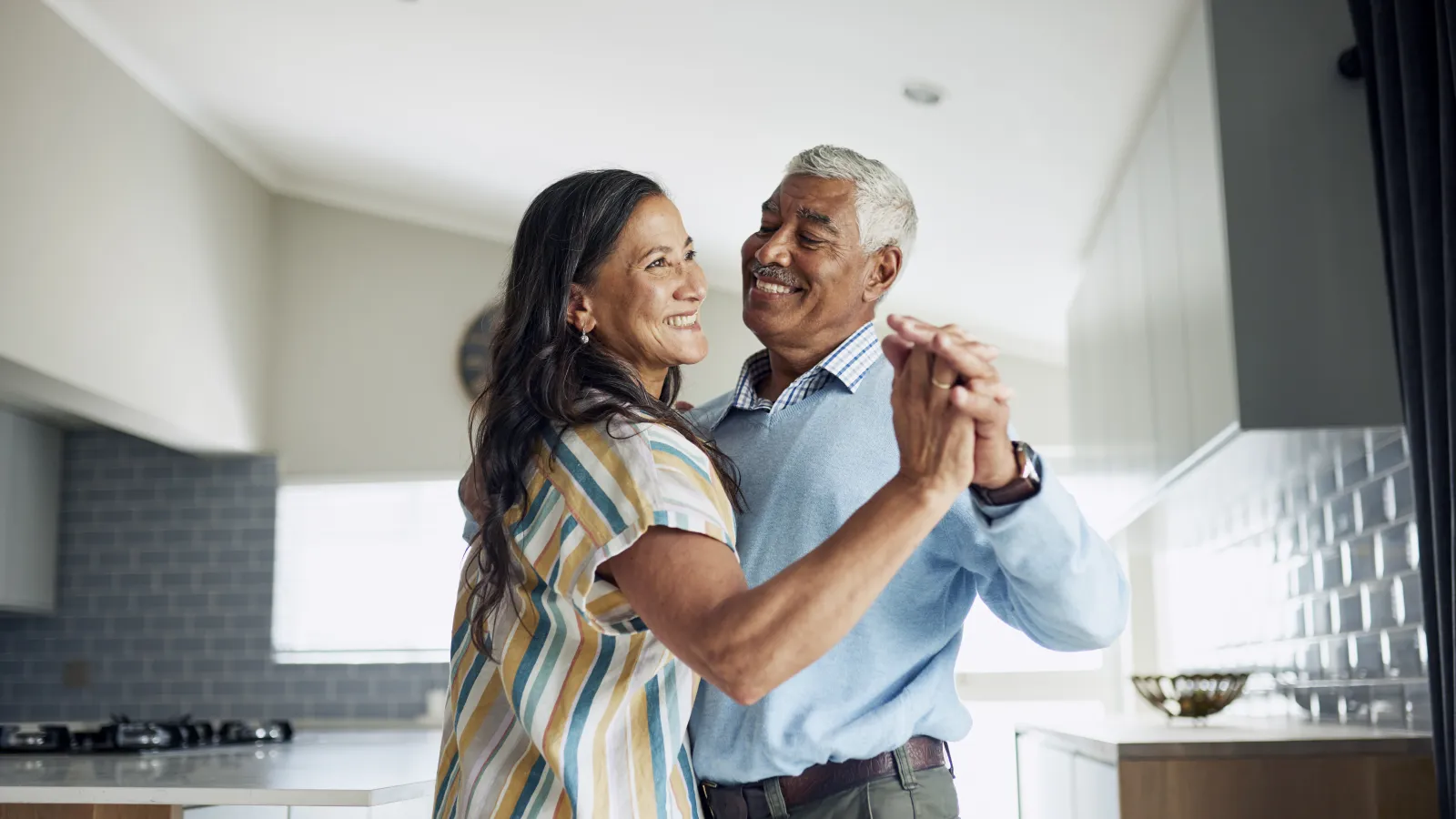 Smiling elderly couple dancing together in a modern bright kitchen, sharing a joyful moment at home.