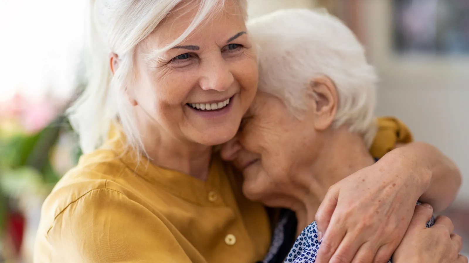 Smiling middle-aged woman warmly hugging an elderly woman showing love and care in a cozy indoor setting