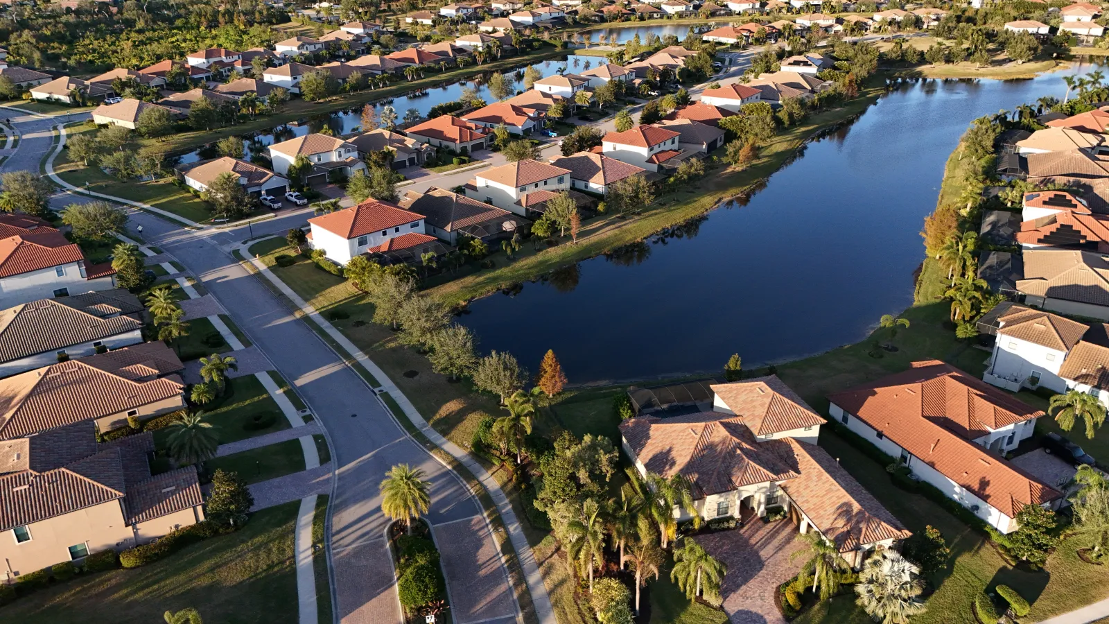 Aerial view of a suburban neighborhood with houses, roads, and water canals on a sunny day.