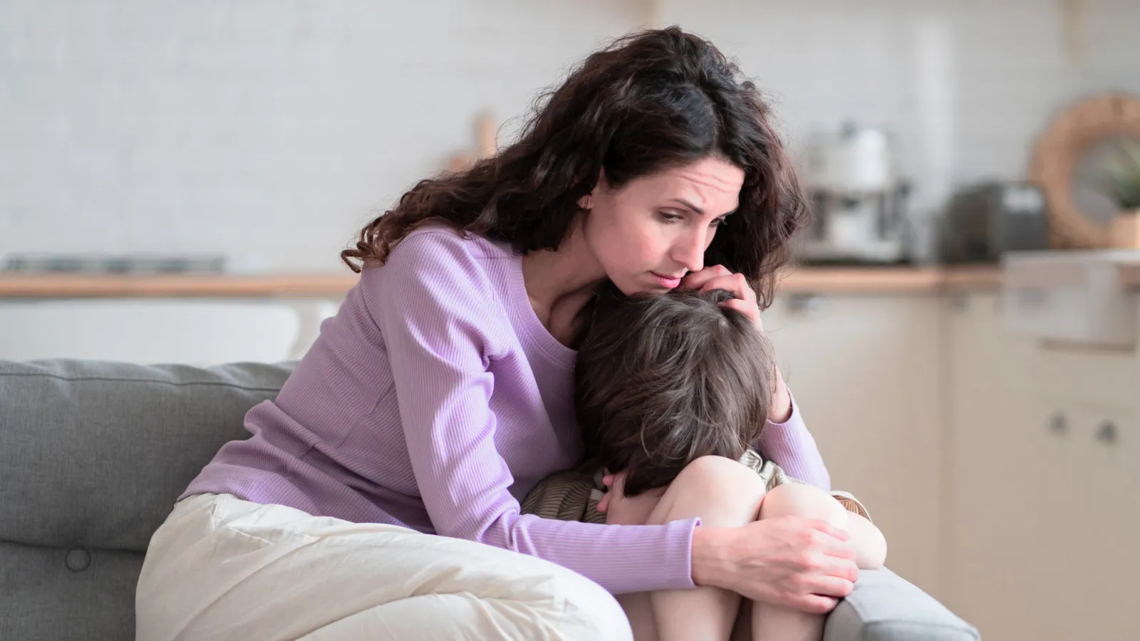 Concerned mother comforting sad child on couch in modern living room