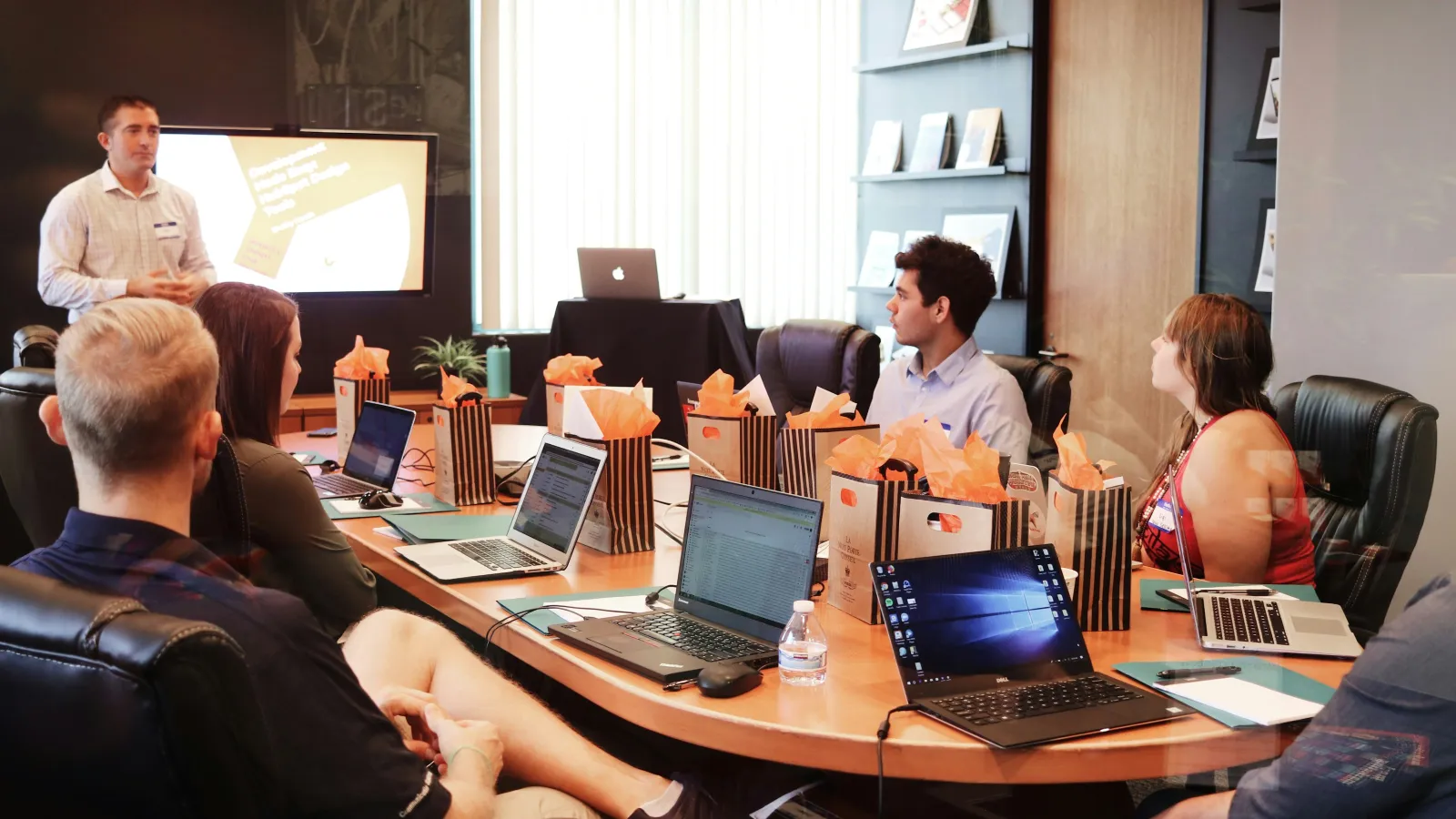 Business team engaged in a meeting around a conference table with laptops and gift bags.