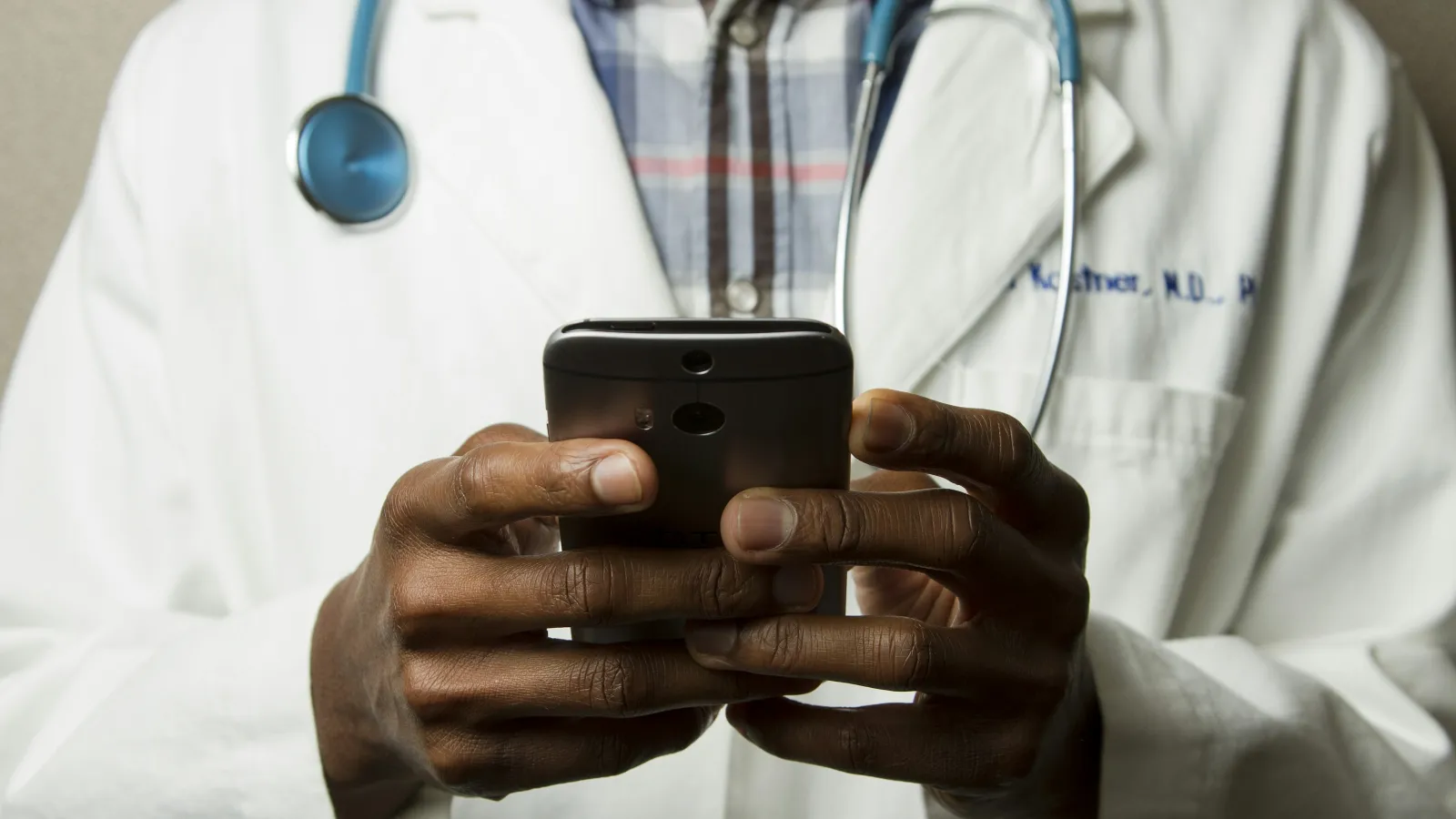 A doctor in a white coat checks a smartphone, symbolizing modern healthcare communication.