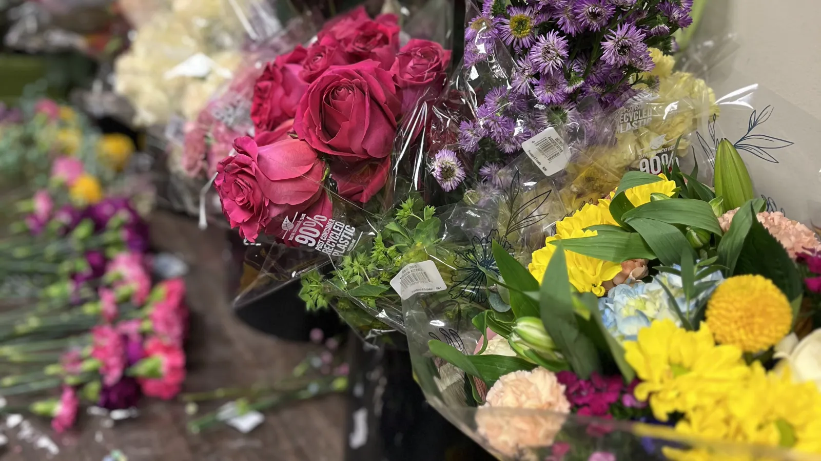 Colorful variety of fresh flowers including roses, chrysanthemums, and asters arranged in bouquets on a table.