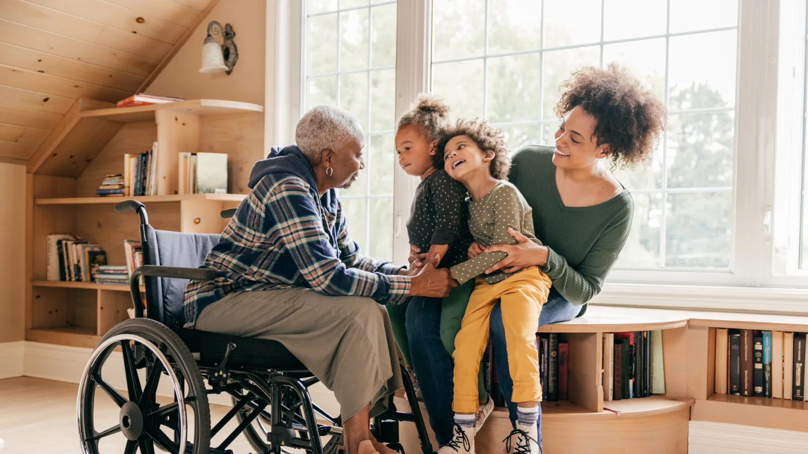 Elderly woman in wheelchair joyfully interacting with children and adult in cozy home with large windows.