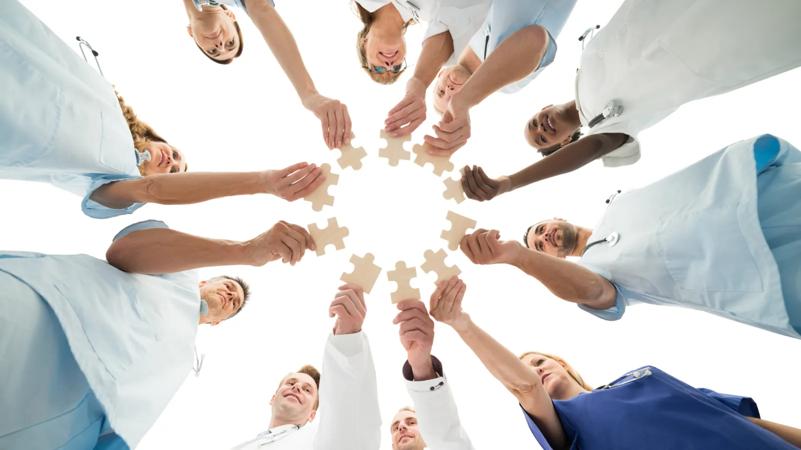 Medical team in scrubs and lab coats holding puzzle pieces together in a circle symbolizing teamwork.