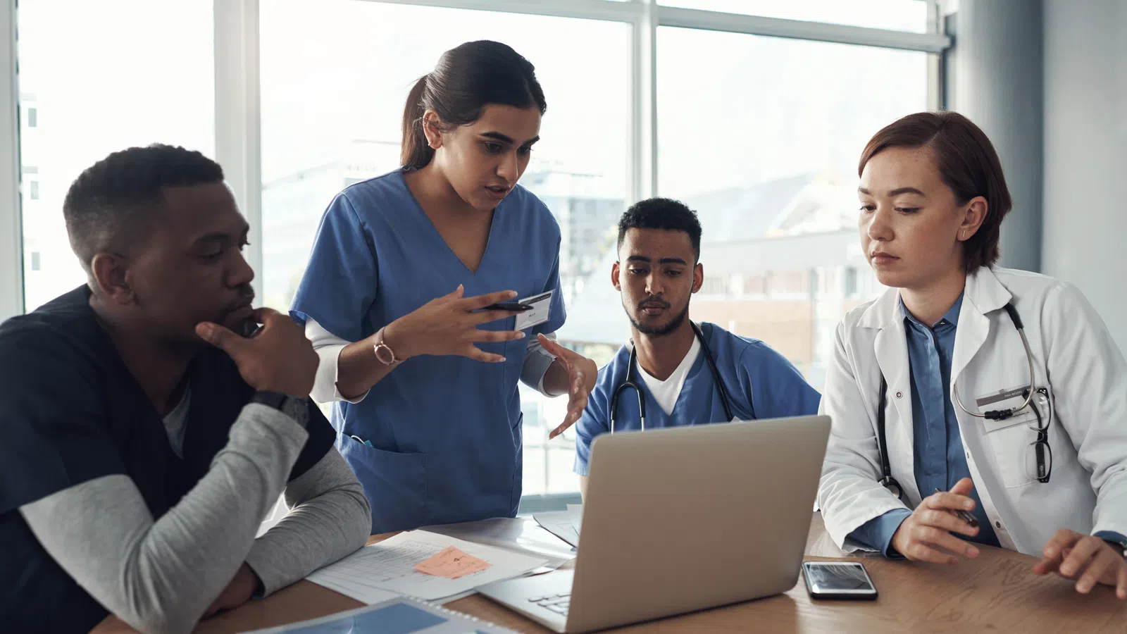 Four medical professionals collaborating around a laptop in a modern workspace.