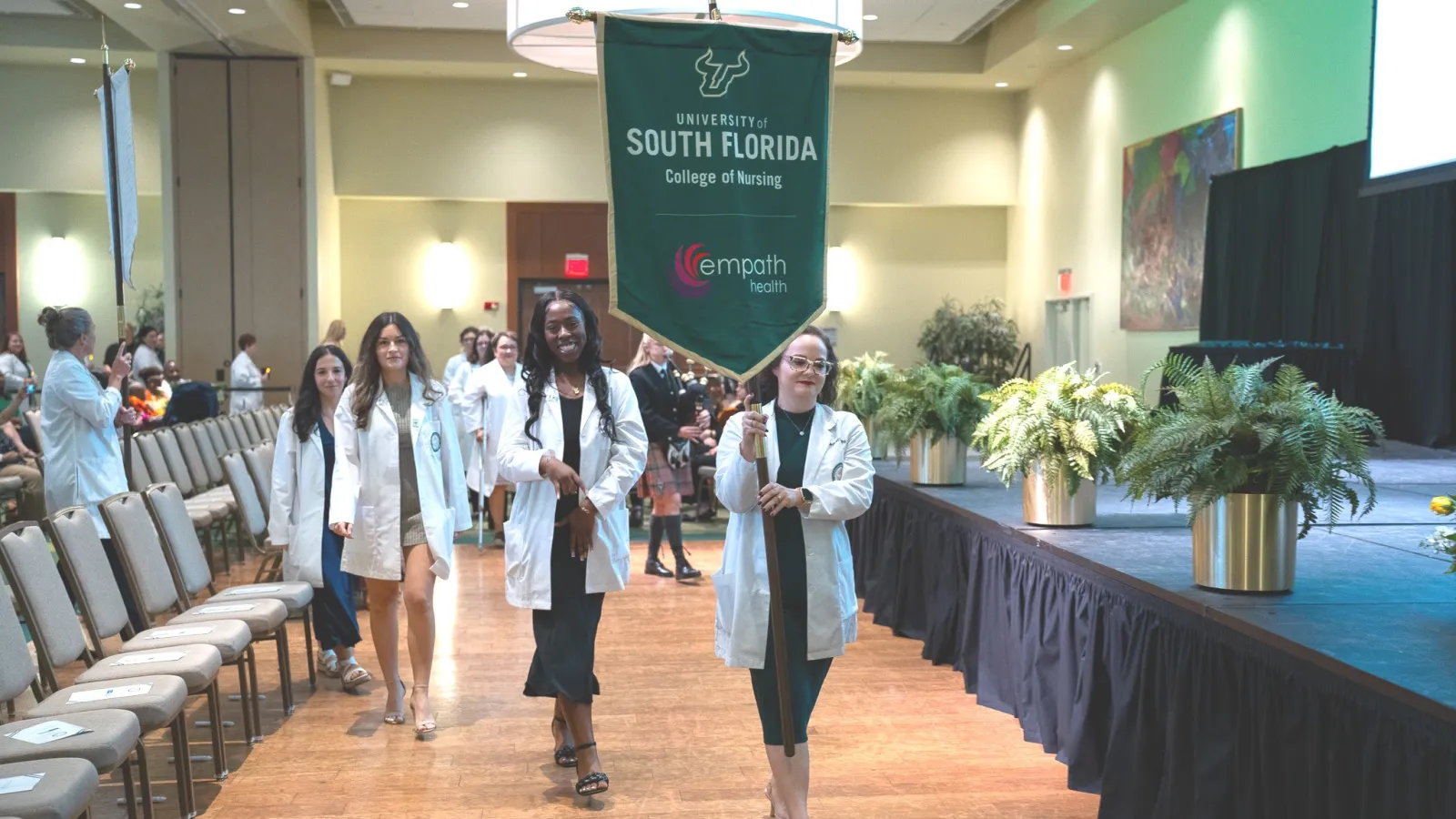 University of South Florida College of Nursing students in white coats process at a formal academic event indoors