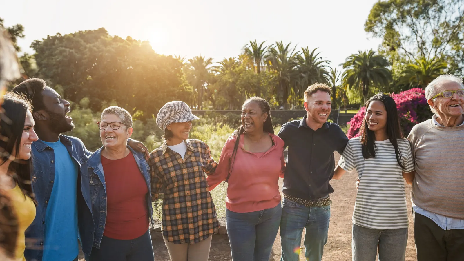 Diverse group of smiling people linked arm in arm outdoors with sunlight and palm trees in the background