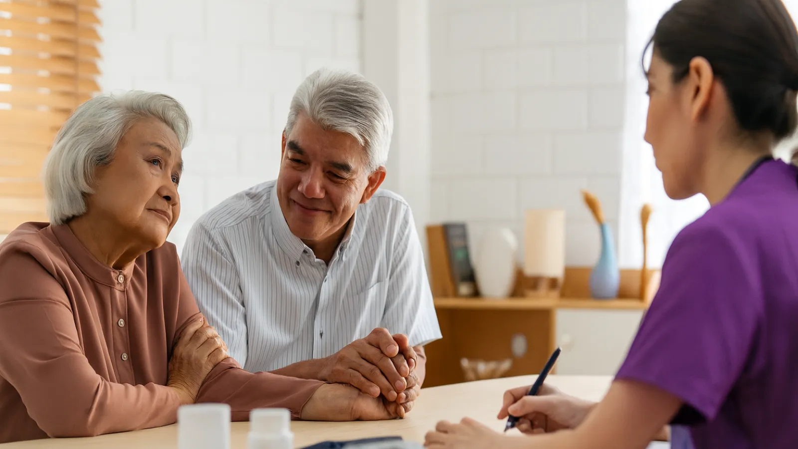 Elderly couple holding hands talking to healthcare professional at medical consultation desk.
