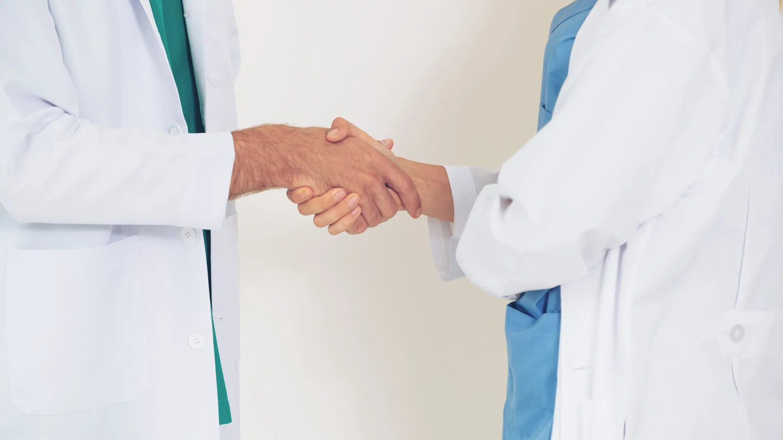 Two healthcare professionals in white coats shaking hands in a clinical setting.