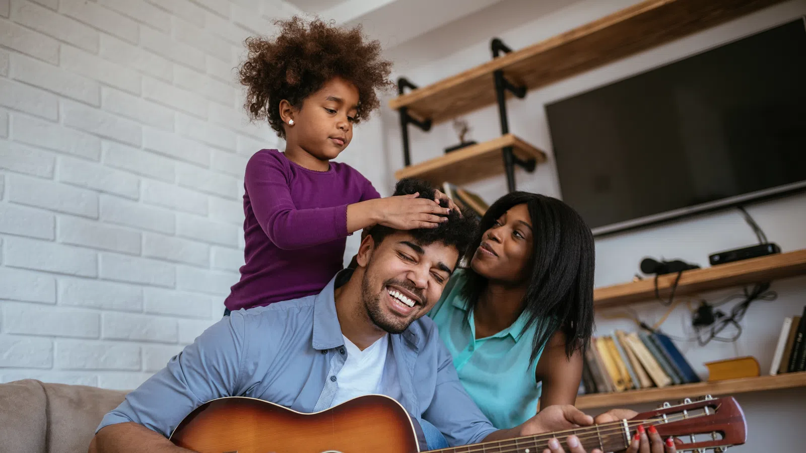 Cherished family moment with a father playing guitar, daughter and mother smiling together indoors.