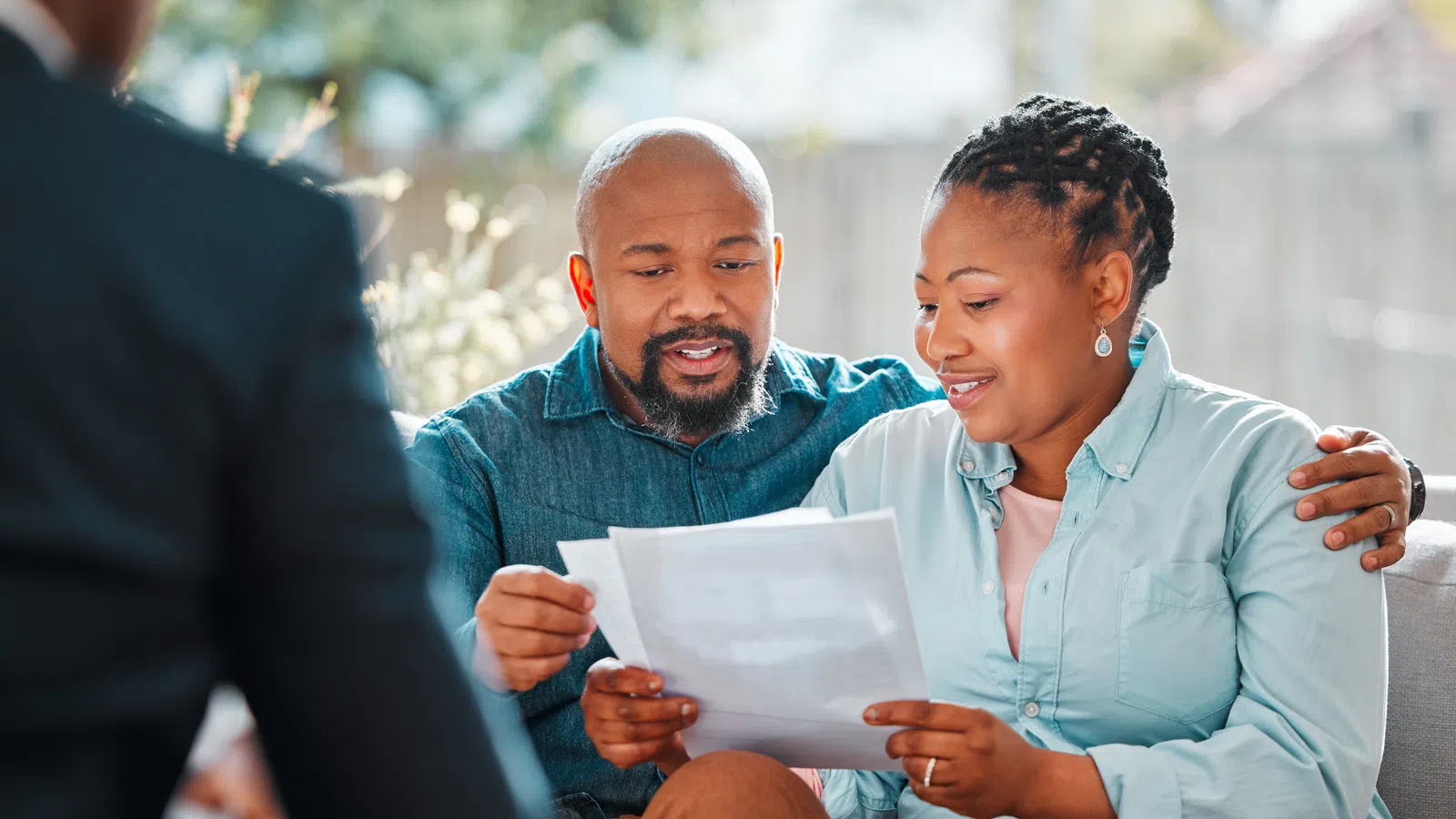 Couple reviewing documents together, smiling, in a warm, inviting living room setting.