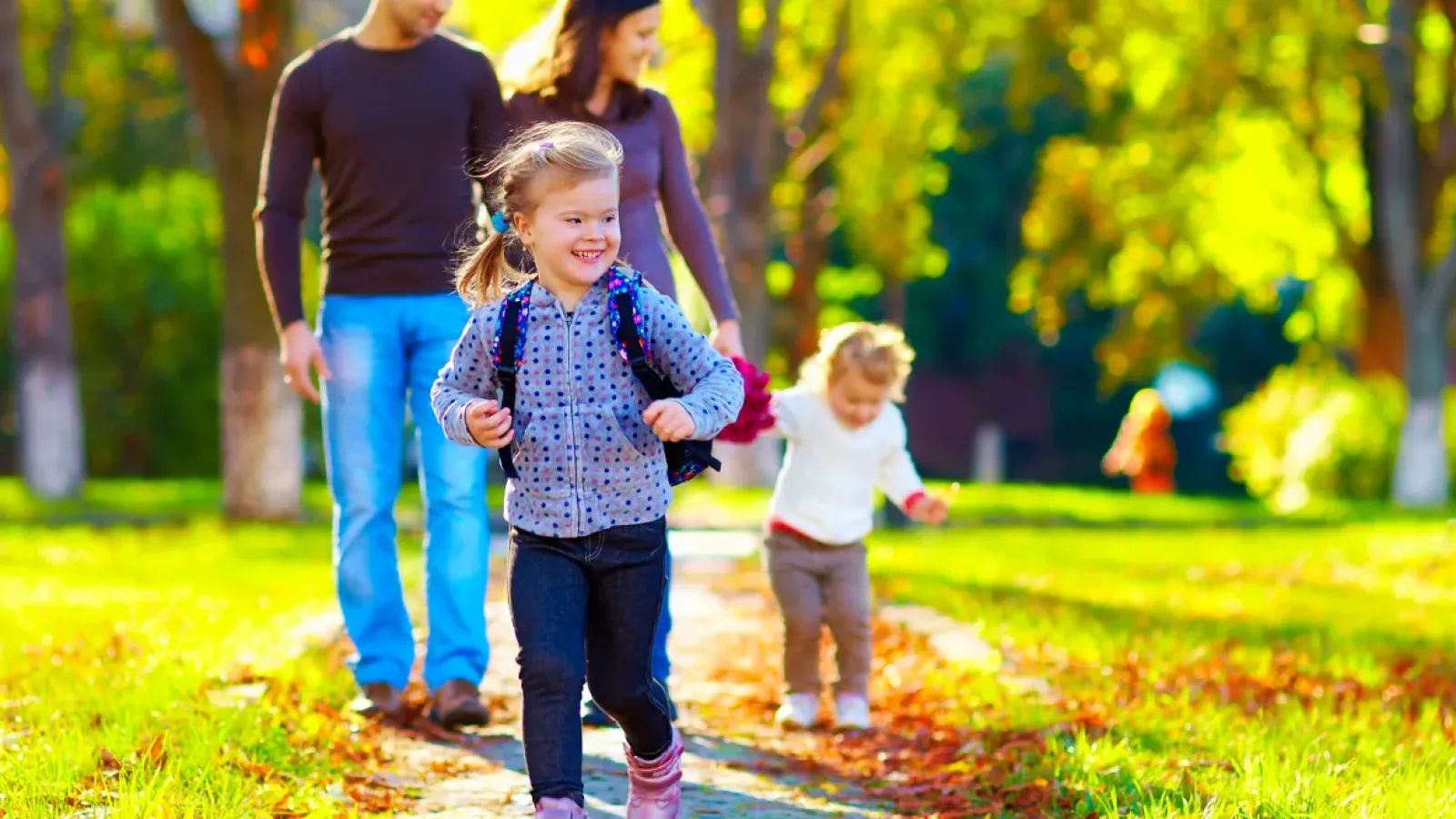 Family enjoying a sunny autumn day walking in the park with children playing and colorful leaves around.