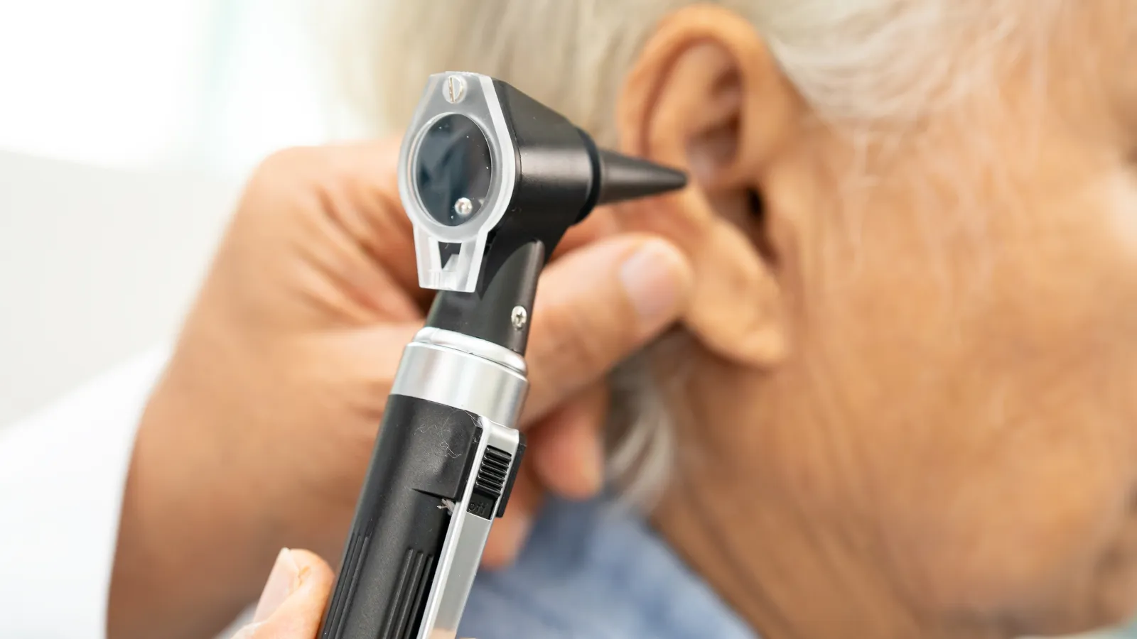 Medical professional examining elderly patient's ear with an otoscope during health checkup.
