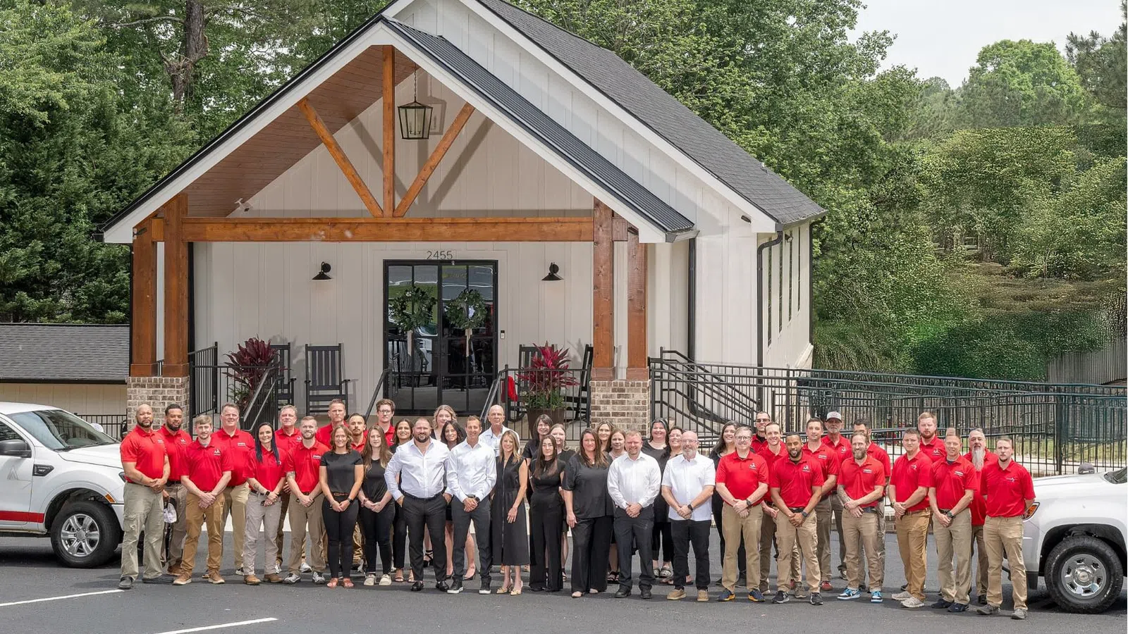 Large team of employees in red and black attire standing outside a modern building with company trucks parked nearby.