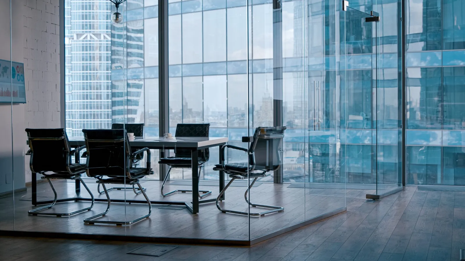 Modern glass-walled conference room with black chairs and city skyscraper views through large windows.