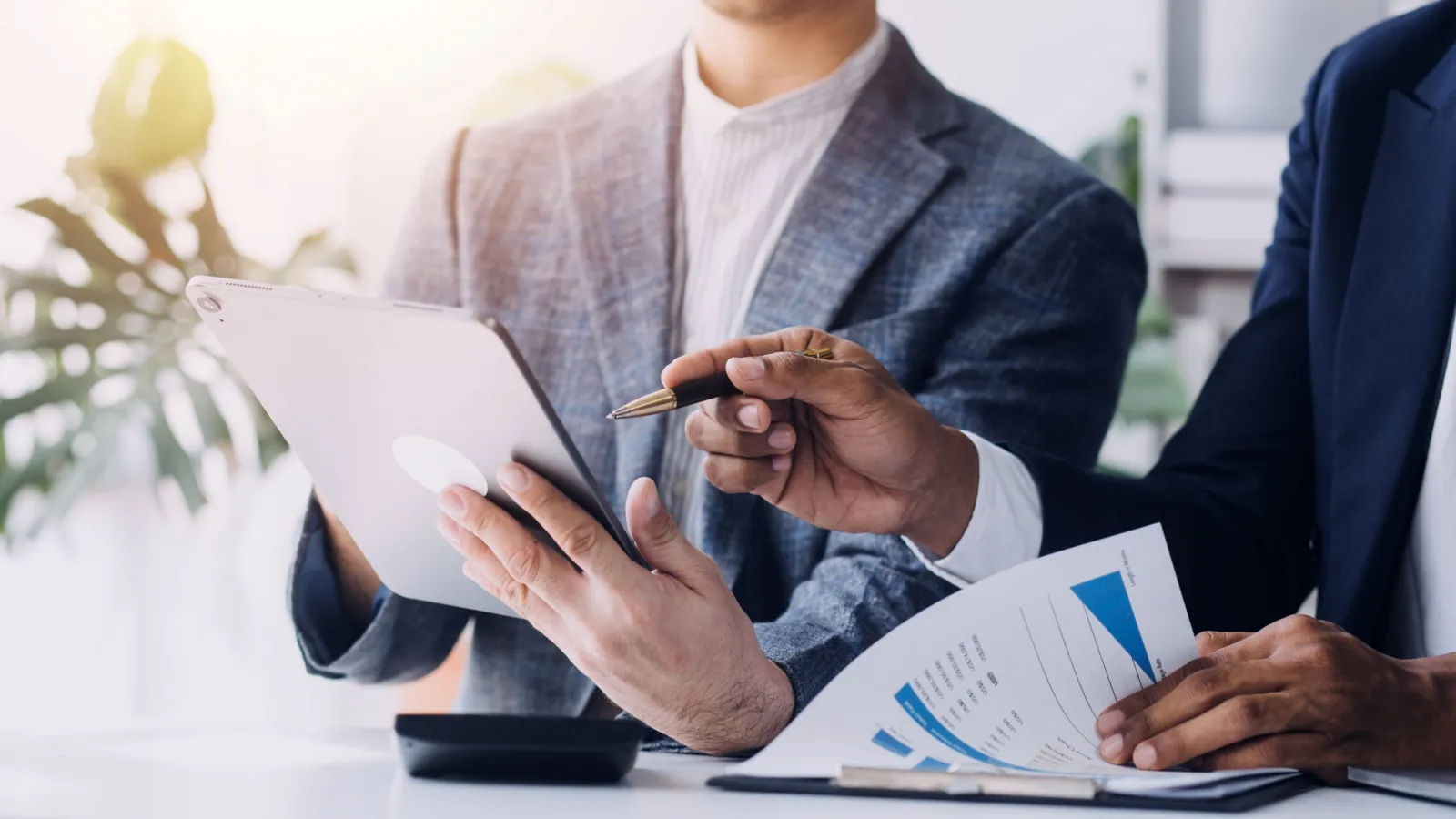 Two business professionals reviewing charts and data on a tablet and paper in a bright office setting
