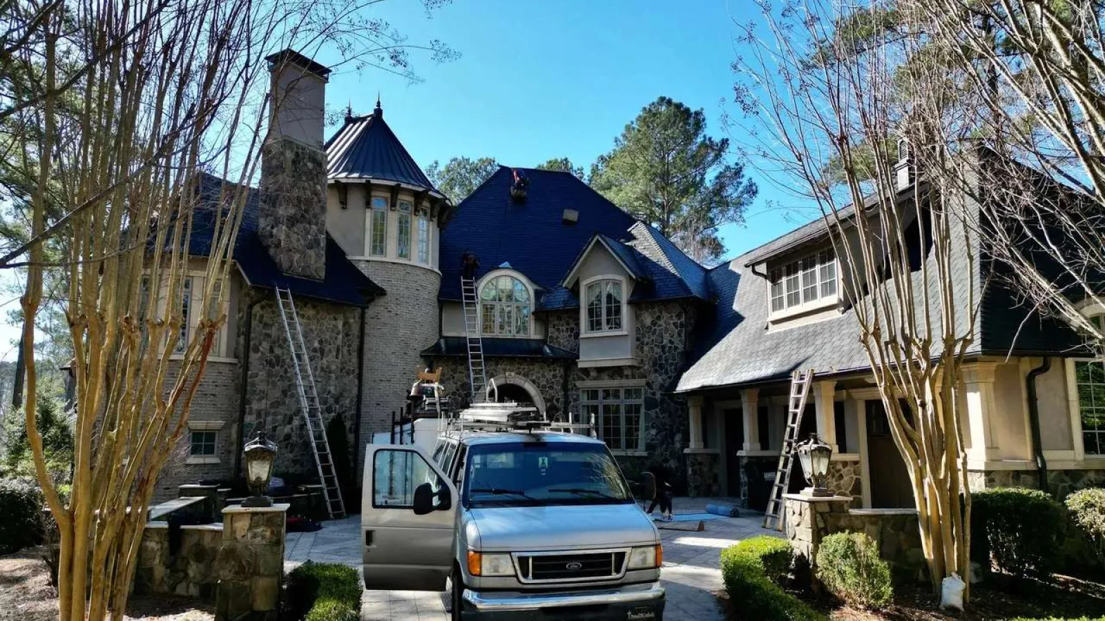 Stone and brick luxury house with ladders, a gray van parked in front.