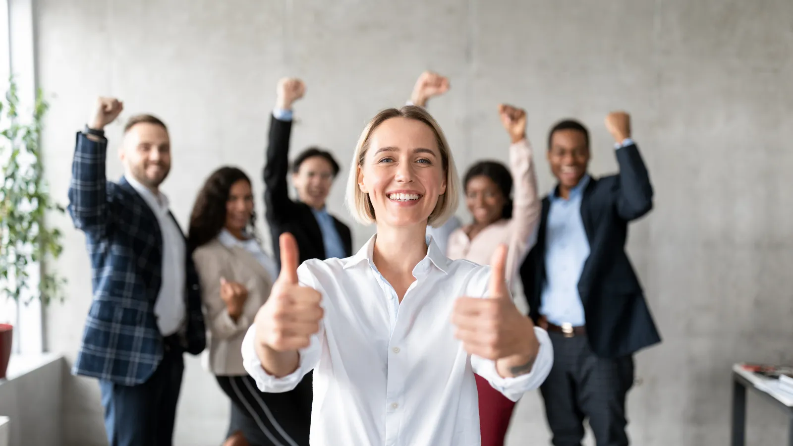 Smiling businesswoman giving thumbs up with diverse team celebrating success in modern office.