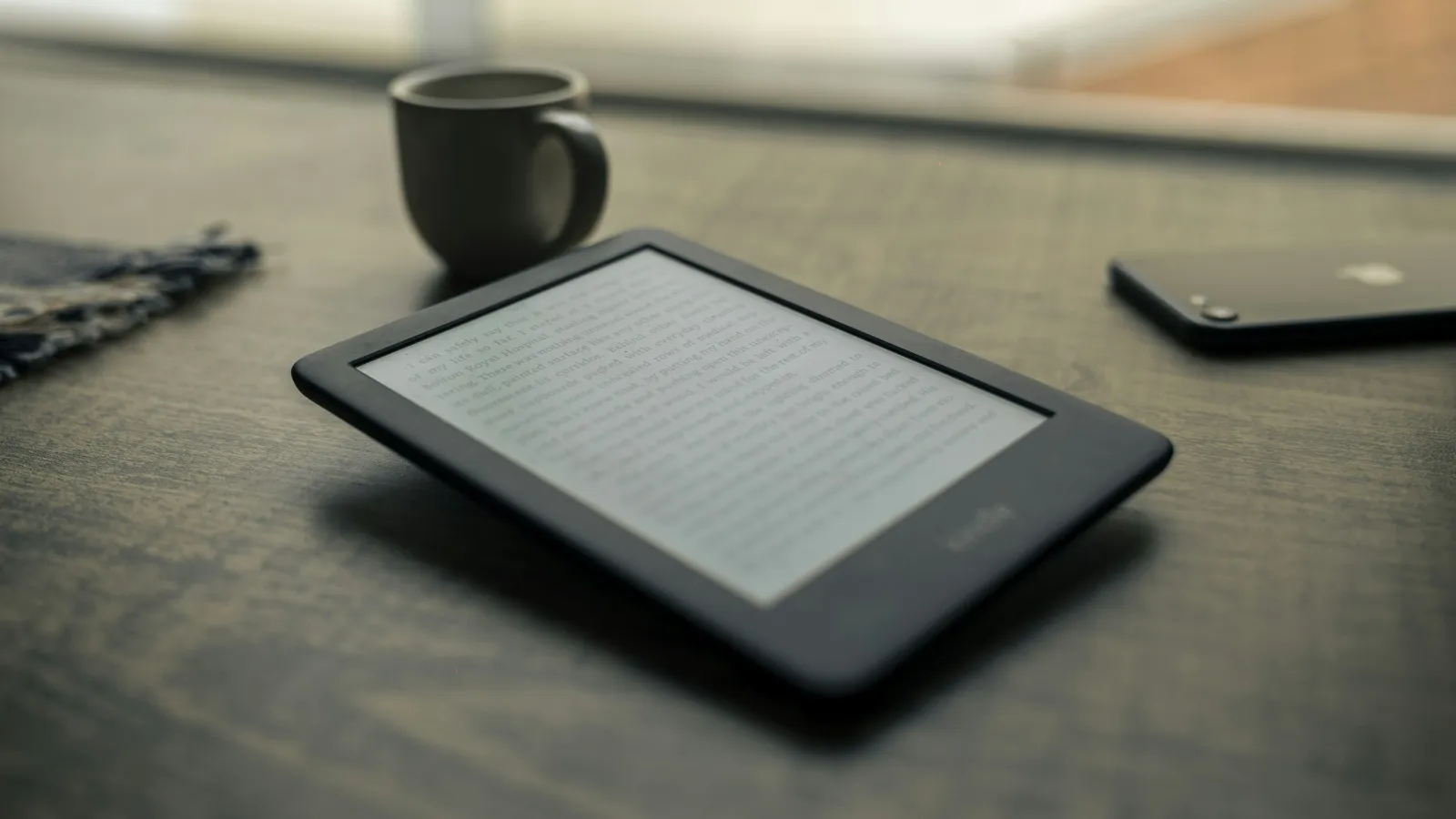 E-reader displaying text on wooden table next to smartphone and coffee cup in soft natural light
