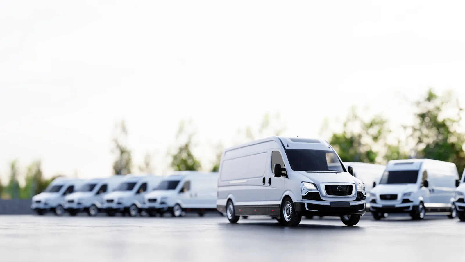 Fleet of white cargo vans parked in a row on a concrete surface with trees in the background under bright sky.