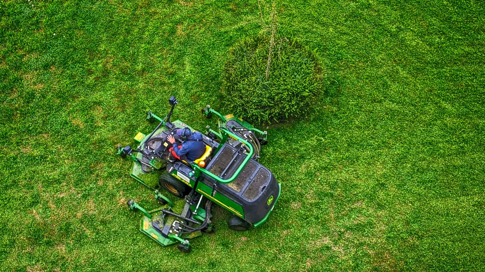 Aerial view of a person operating a green tractor mowing a large grassy field on a sunny day