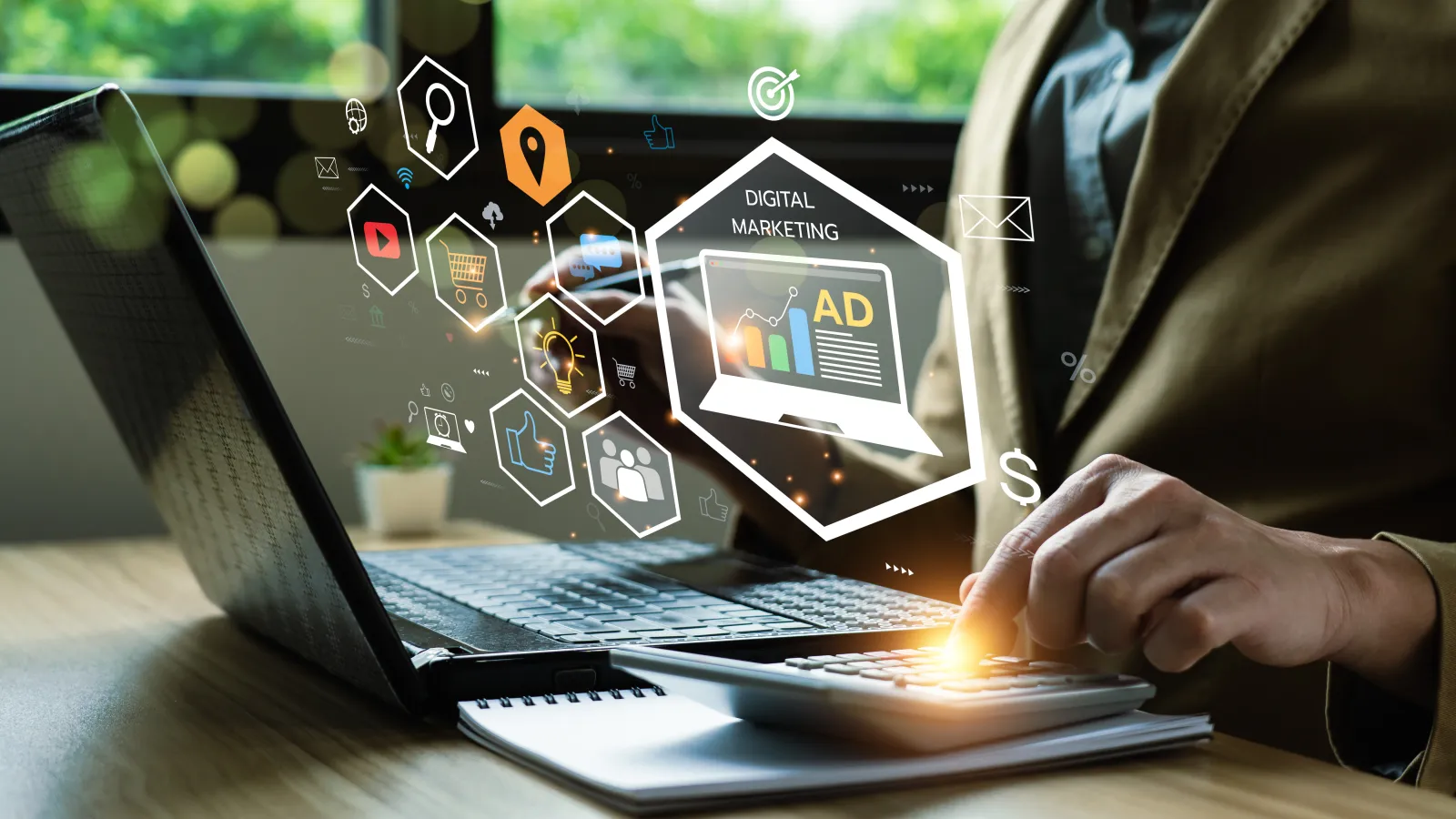 Person using calculator and laptop with digital marketing icons floating above the devices