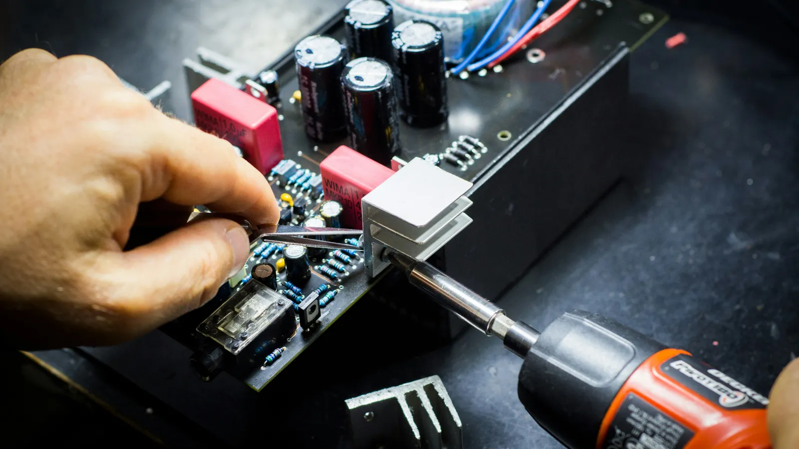 Close-up of a person soldering electronic components on a circuit board with a soldering iron and tweezers.
