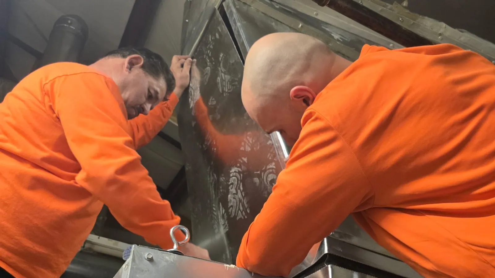 Two Estes workers in orange uniform installing HVAC equipment inside a school in atlanta