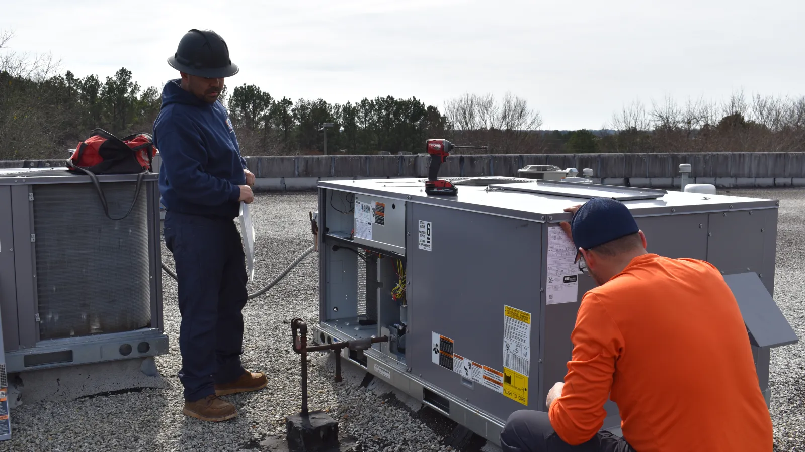 Two technicians Estes Commercial Services inspecting and repairing rooftop HVAC units on a commercial building.